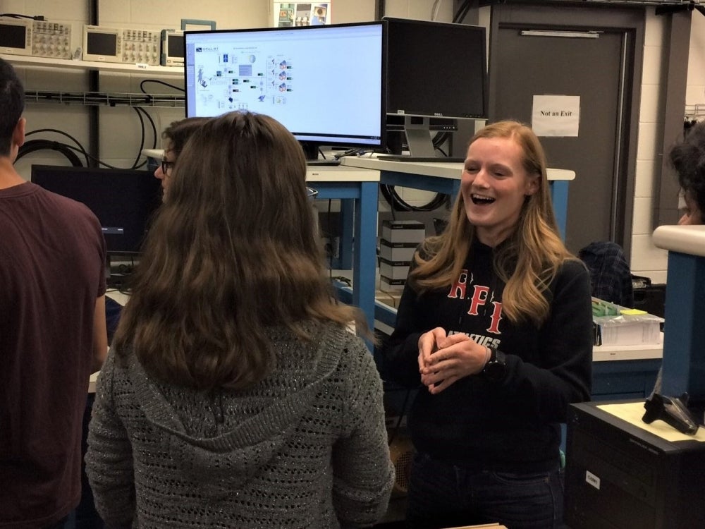 A young woman in an RPI sweatshirt is smiling at a group of people with their backs to the camera.